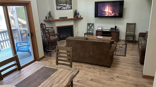Ein Wohnzimmer mit Kamin, einem an der Wand montierten Fernseher und einer Essecke mit Tisch und Stühlen.