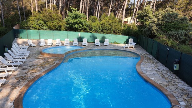 A swimming pool with a stone border, surrounded by white lounge chairs and a green fence. - Studio with private garden (Sanary-sur-Mer)
