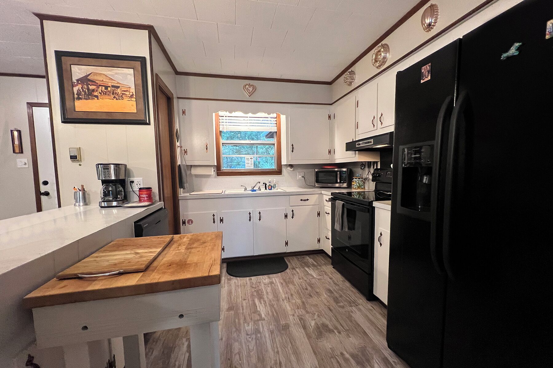 A compact kitchen with white cabinets, a black refrigerator, a microwave, and a coffee maker.