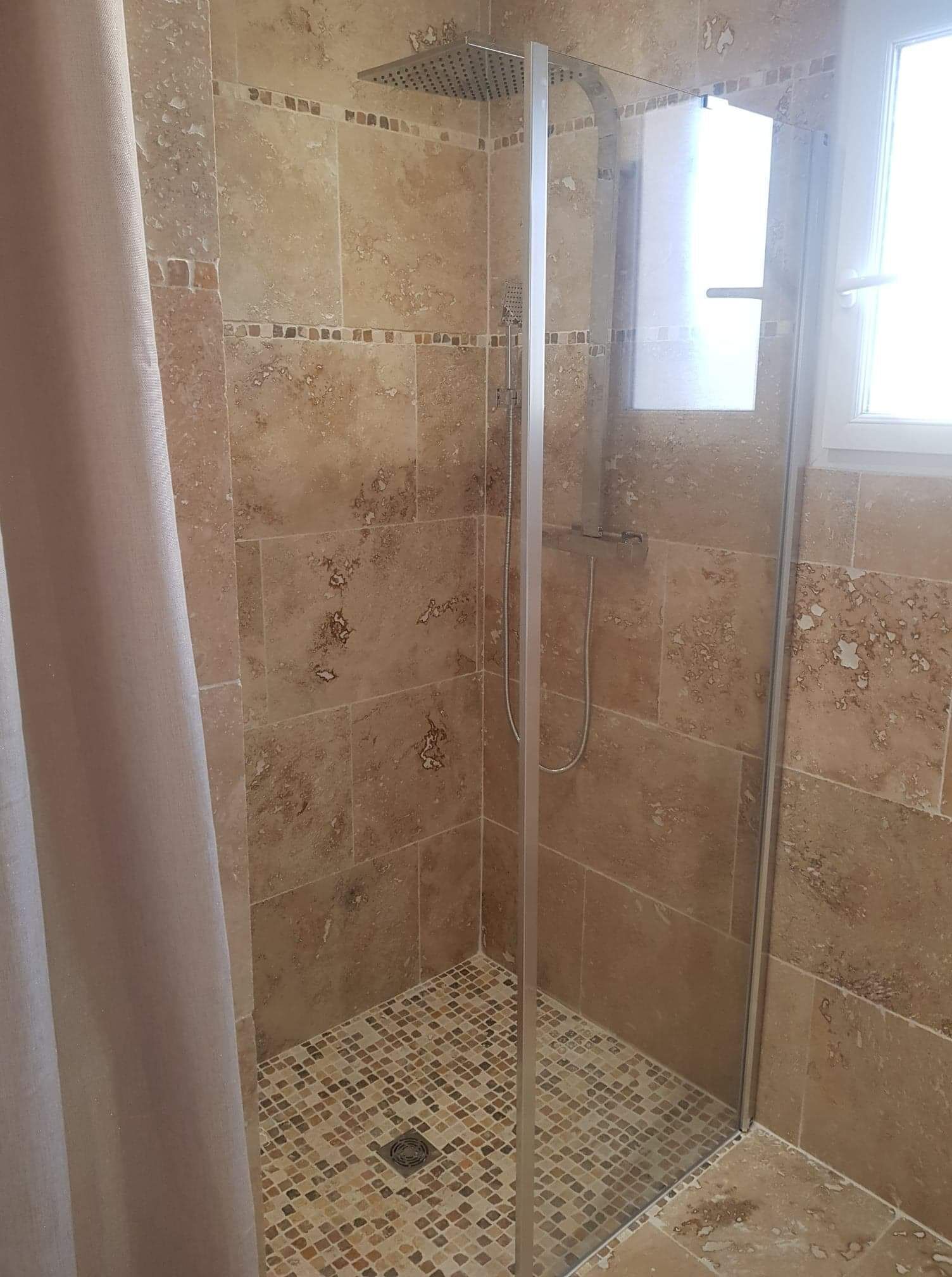 A glass-enclosed shower with a tiled floor and a showerhead.