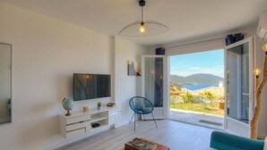 A modern living room with a large TV, a blue chair, and a view of the sea through large glass doors. - T2 ground floor villa Magnificent sea view (Villanova)