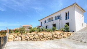 A modern two-story house with a stone retaining wall and a clear blue sky. - T2 ground floor villa Magnificent sea view (Villanova)