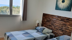 Un dormitori amb dos llits, un capçal de fusta, un llum penjant, una finestra amb cortines i una obra d'art penjada a la paret.
