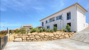 Una casa moderna de dos pisos amb un mur de pedra de sostre, un vial de formigó i un cel blau clar.