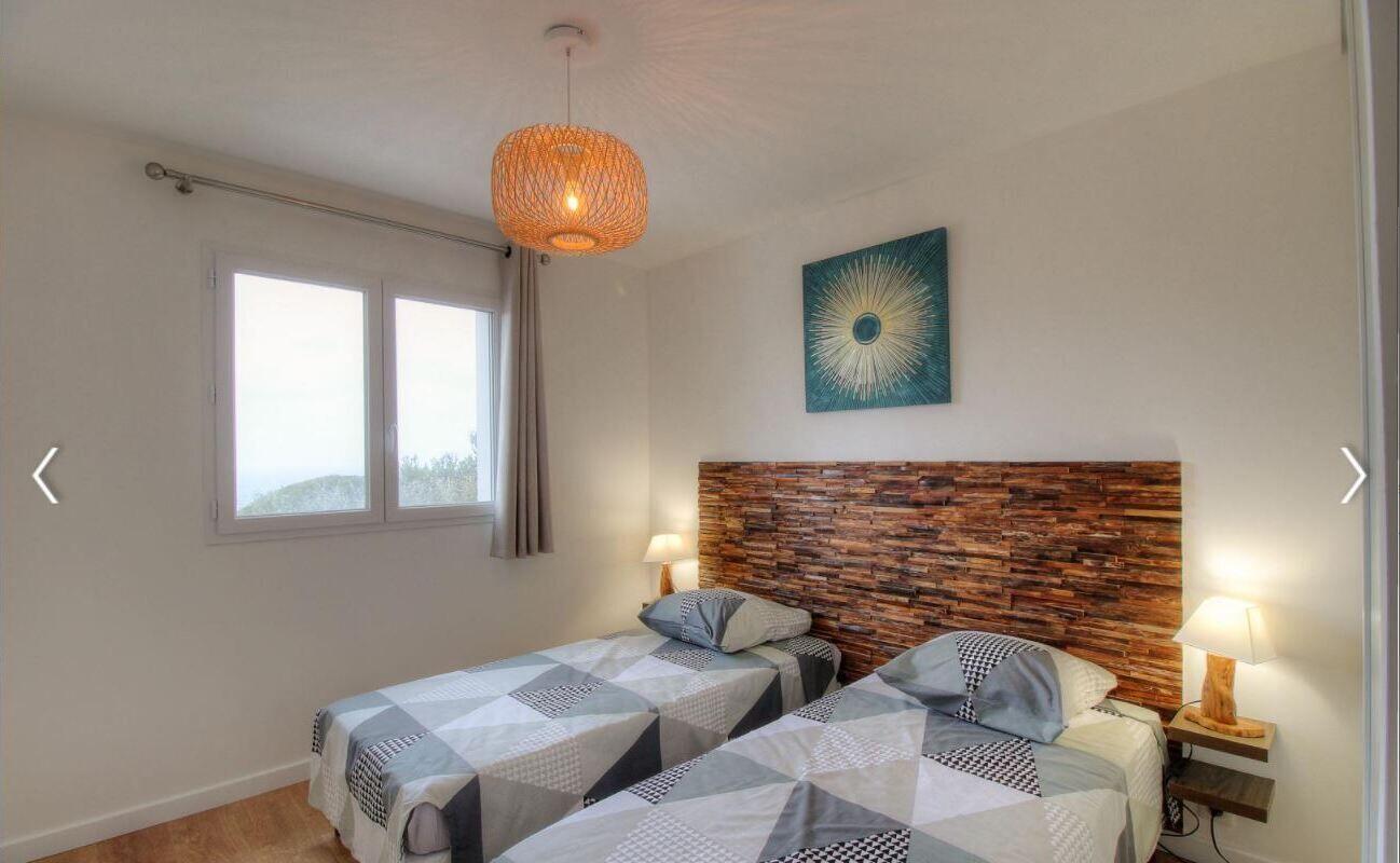 Une chambre avec deux lits, une tête de lit en bois, un luminaire suspendu, une fenêtre et une œuvre d’art murale.
