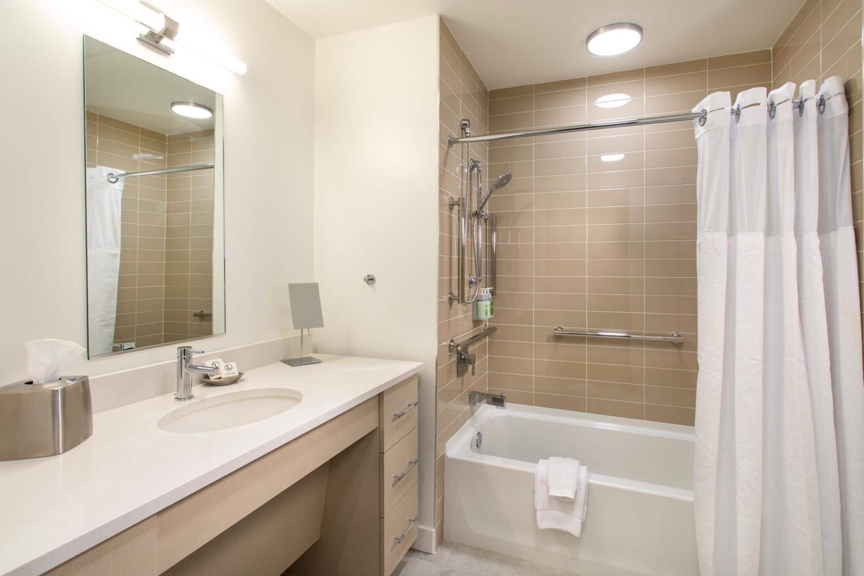 A modern bathroom with a large mirror, a sink, a bathtub, and a shower area.