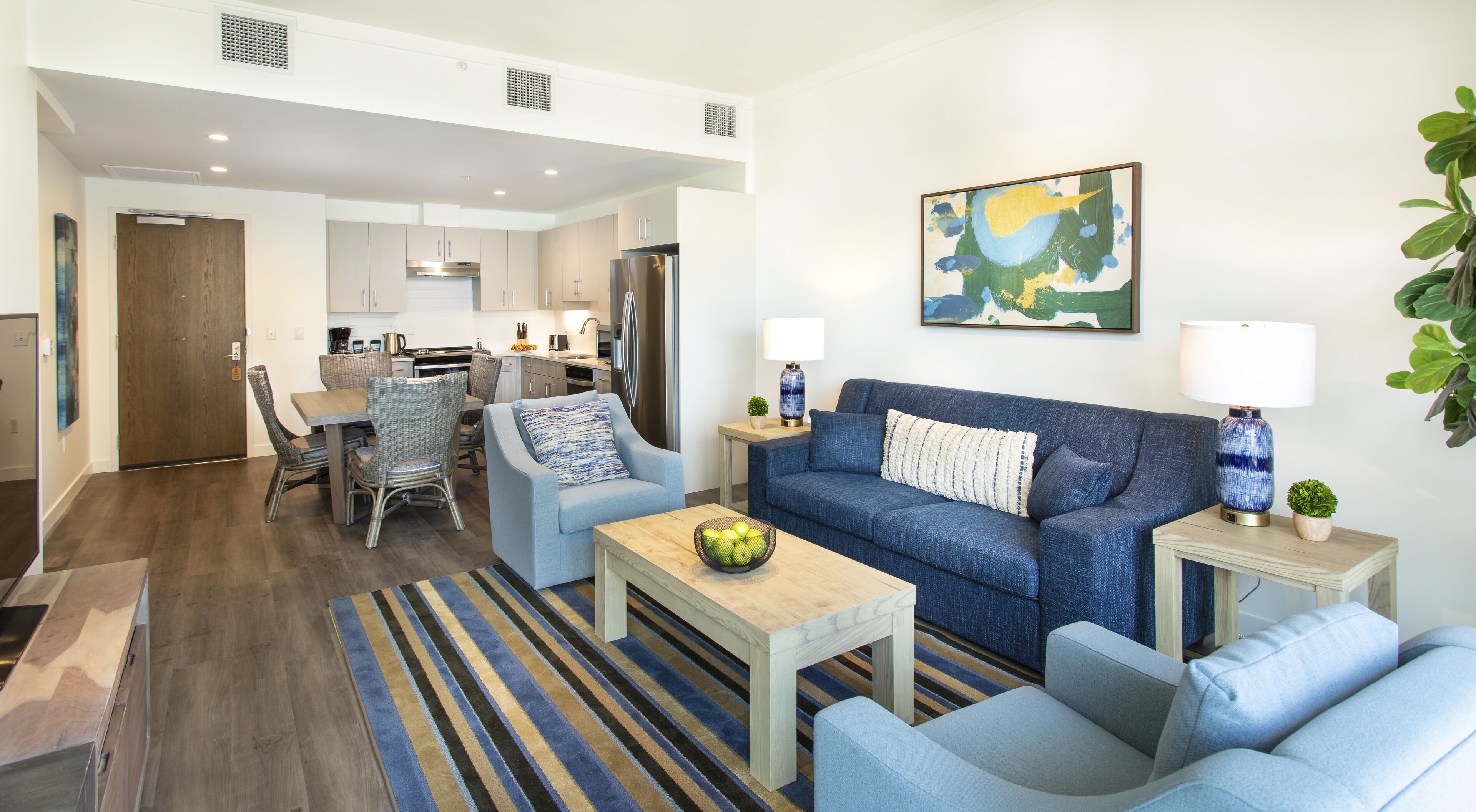 A modern living room with a blue sofa, two armchairs, a coffee table, and a dining area with a wooden table and chairs.