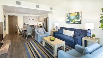A modern living room with a blue sofa, two armchairs, a coffee table, and a dining area with a wooden table and chairs.