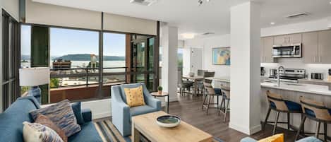 A modern living room with a sofa set, a coffee table, and a view of a balcony with a cityscape and water.