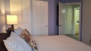 A bedroom with a bed, pillows, a nightstand, a lamp, and a door leading to another room.