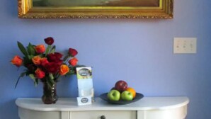 A white console table with a vase of flowers, a bowl of fruit, and a framed painting on the wall.