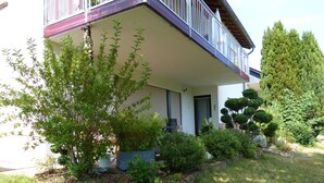 A two-story house with a balcony, surrounded by various plants and trees. - Ferienwohnung Schöne Aussicht (Weilrod)
