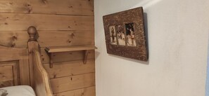 Ein hölzernes Bett mit Kopfteil, ein kleines Holzregal und ein an der Wand befestigter Bilderrahmen.