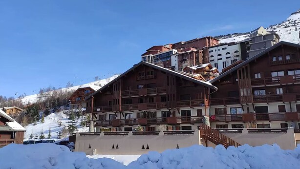 Un albergo con una pista da sci sullo sfondo, architettura in legno e un cielo azzurro limpido.
