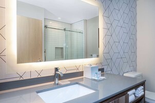 A modern bathroom with a large mirror, a sink, and a shower.