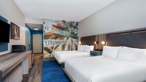 A hotel room with two beds, a TV, a desk, and a mural with palm trees and text.