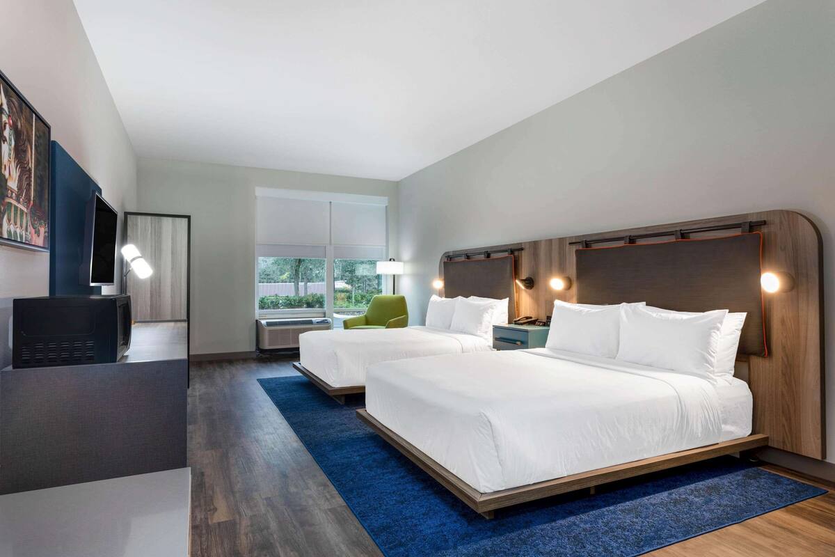 Una habitación de hotel moderna con dos camas, un escritorio, una silla y un ventanal grande.