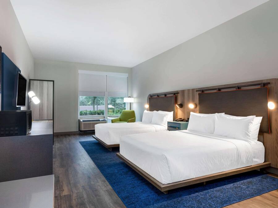 A modern hotel room with two beds, a desk, a chair, and a large window.