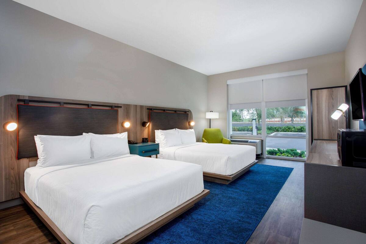 Una habitación de hotel con dos camas, un escritorio, una silla y un televisor.