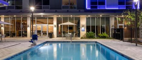 Un hotel moderno con piscina, mobiliario exterior y una fachada bien iluminada.
