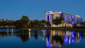 A modern hotel with a reflective pool in front, featuring a prominent tower with illuminated signage.