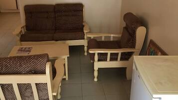 Quarto com sofá, duas poltronas, uma mesinha e um frigorífico.
