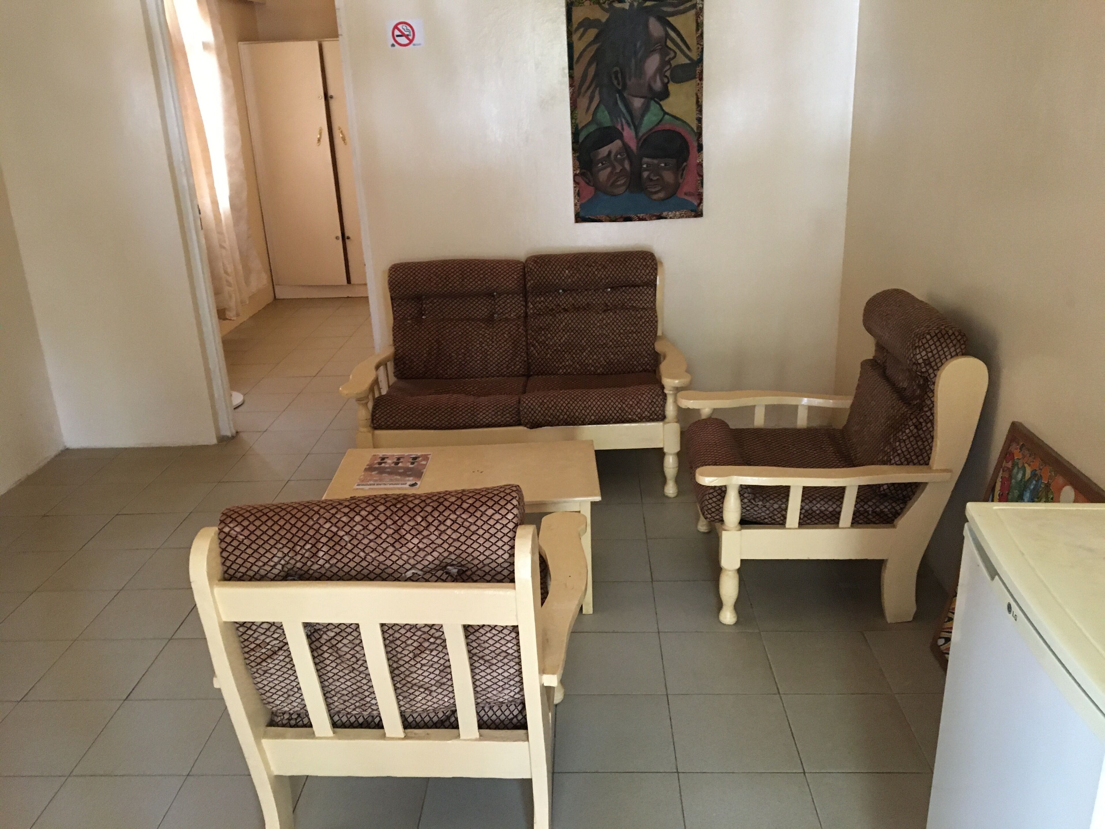 A small living area with a sofa, two armchairs, a table, and a refrigerator.