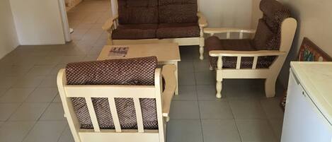 A small living area with a sofa, two armchairs, a table, and a refrigerator.