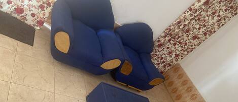 A blue armchair with wooden patches and a matching ottoman on a tiled floor.
