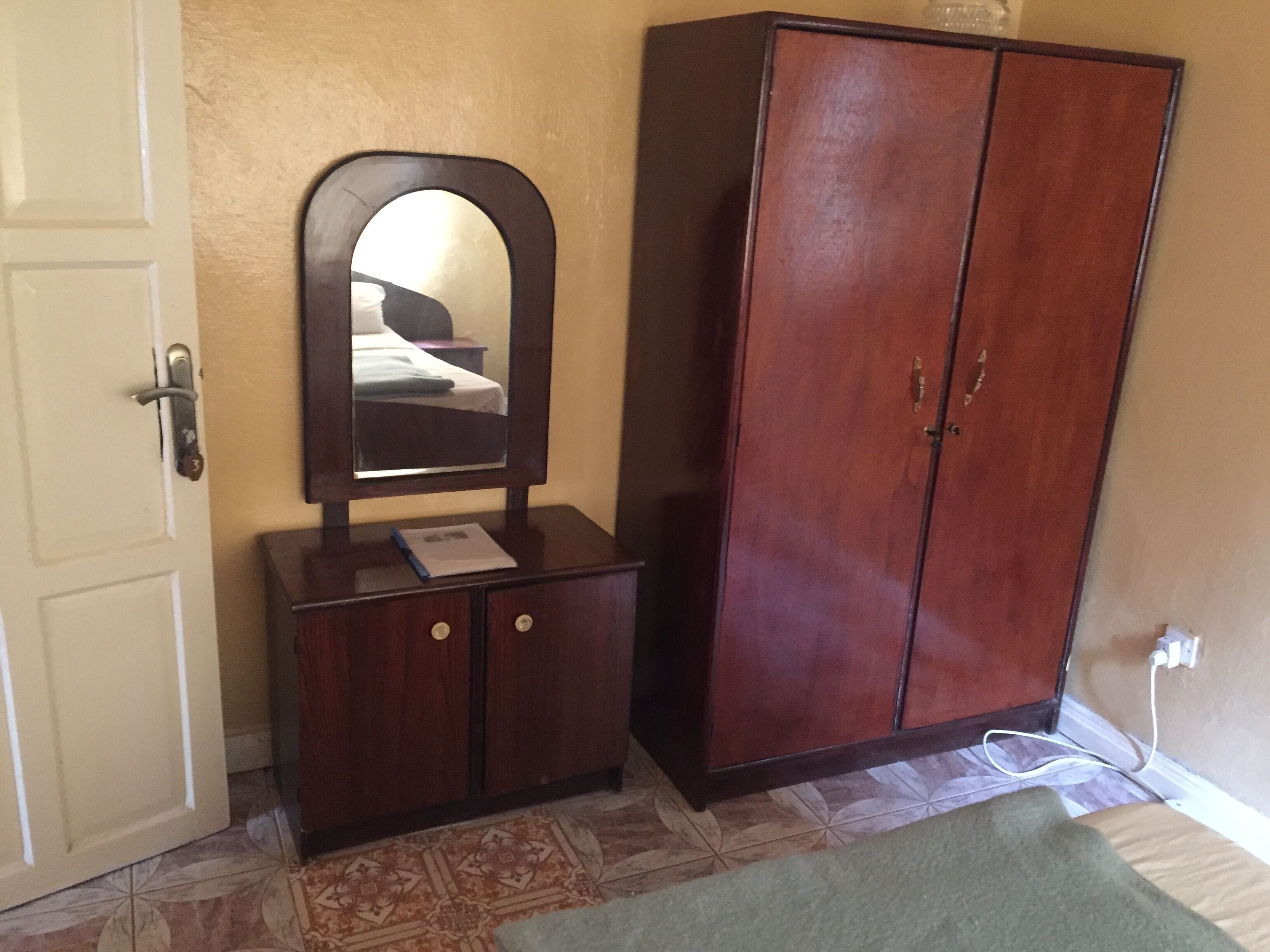 A room with a wooden wardrobe, a mirror, a door, and a patterned floor.