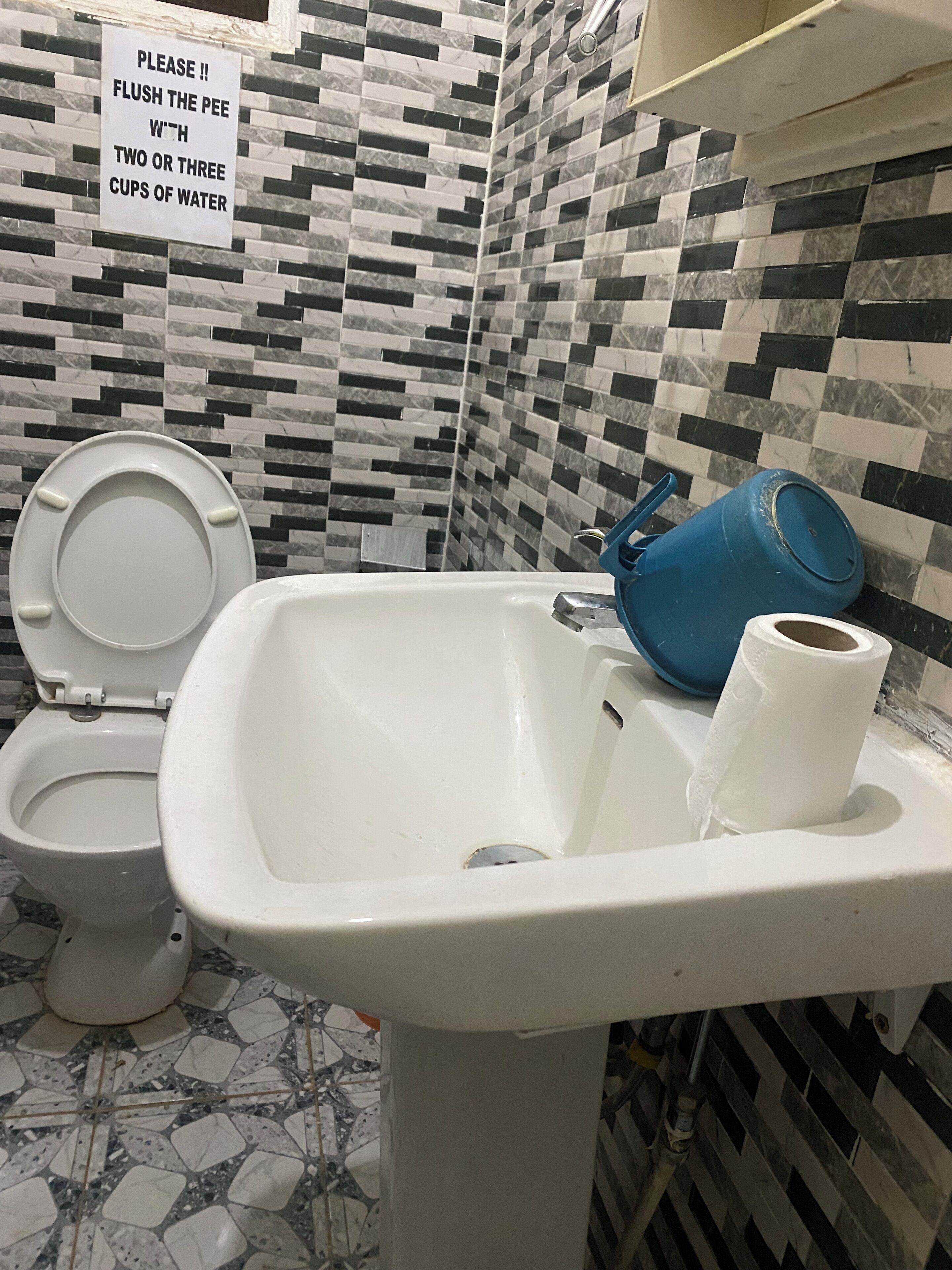 A bathroom with a toilet, sink, and a sign instructing to flush the toilet with two or three cups of water.
