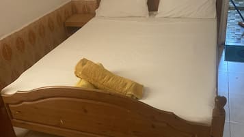 A single bed with a wooden frame and white bedding, a small bedside table, and a wall-mounted light fixture.