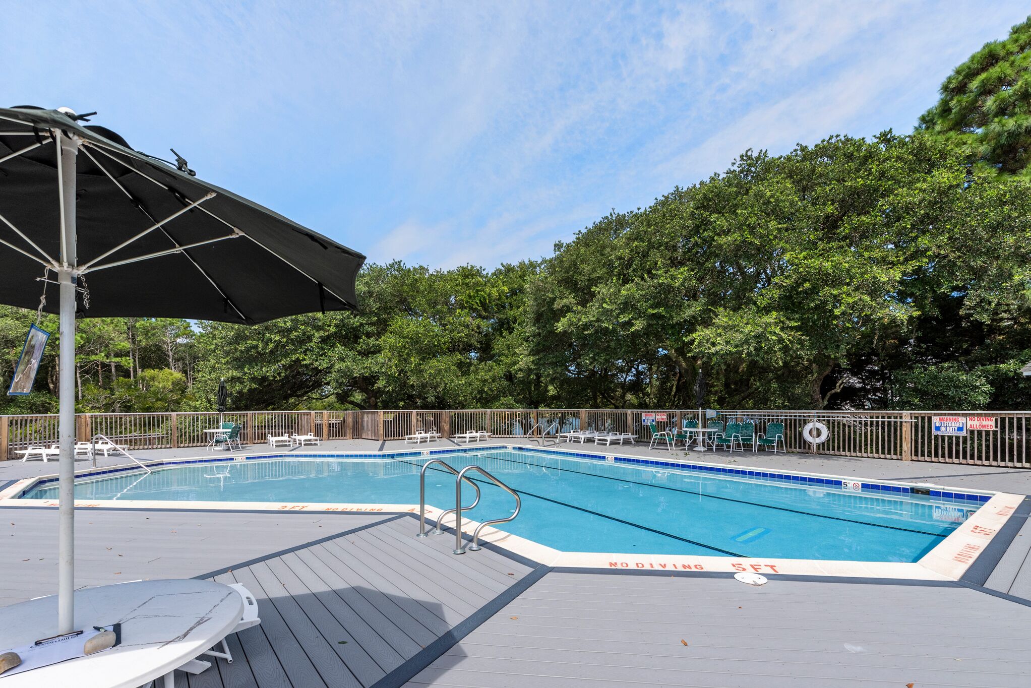 A rectangular swimming pool with a wooden deck, surrounded by lounge chairs and a covered area with a canopy.