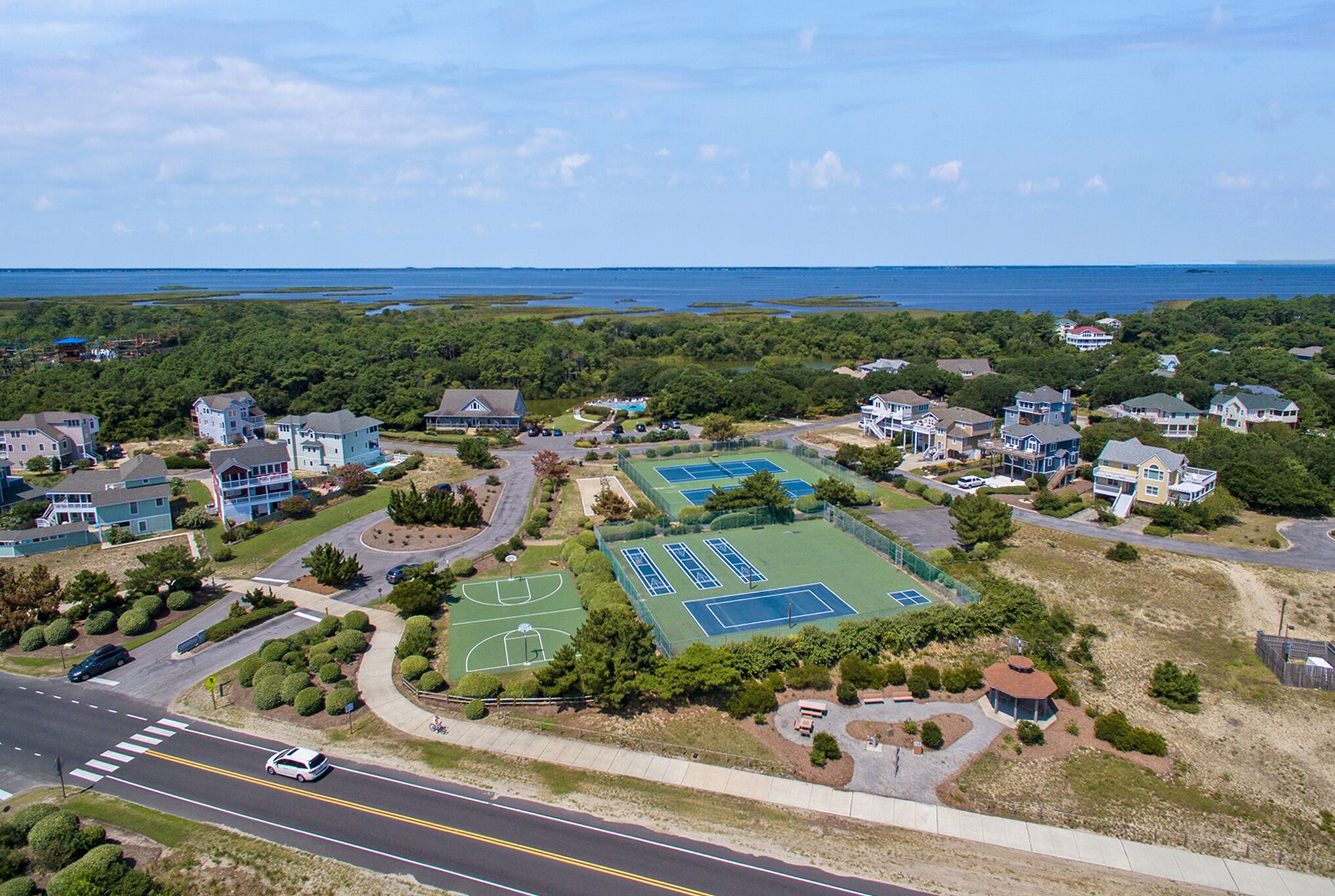 An aerial view of a residential area with houses, a road, and a tennis court complex.