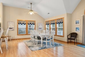 A dining area with a white table and chairs, wooden flooring, and nautical-themed artwork on the walls.