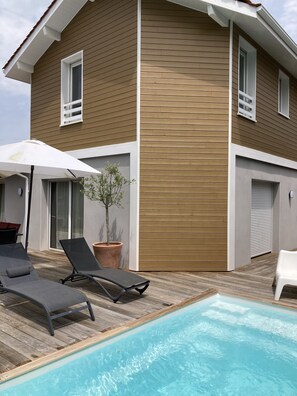A modern house with a wooden exterior, a swimming pool, and outdoor seating. - Charming House (Labenne)
