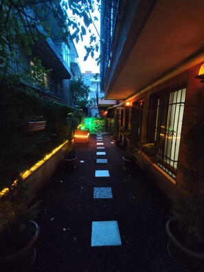 A narrow pathway with stepping stones leading to a brightly lit area with a green light.