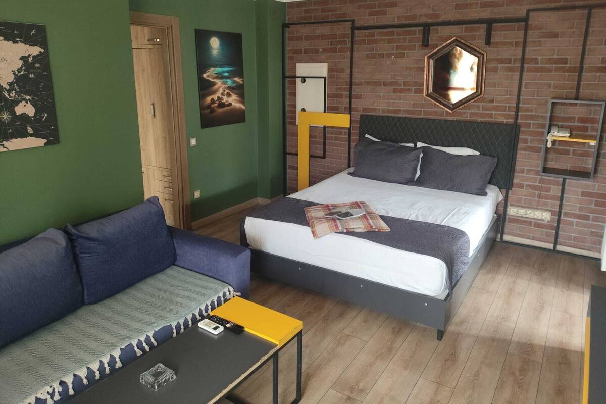 A room with a bed, a sofa, a small table, a map on the wall, and a mirror.