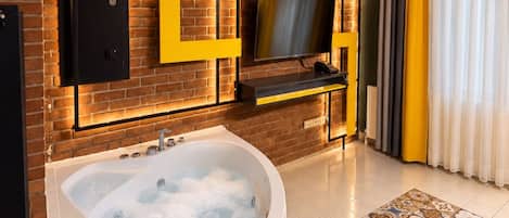 A modern bathroom with a bathtub, a television mounted on the wall, and a brick wall.