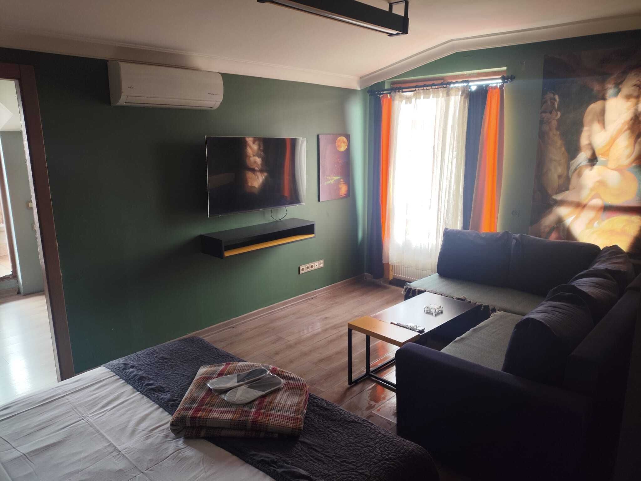 A living room with a flat-screen TV, a sofa, a coffee table, and a bed.