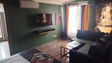 A living room with a flat-screen TV, a sofa, a coffee table, and a bed.
