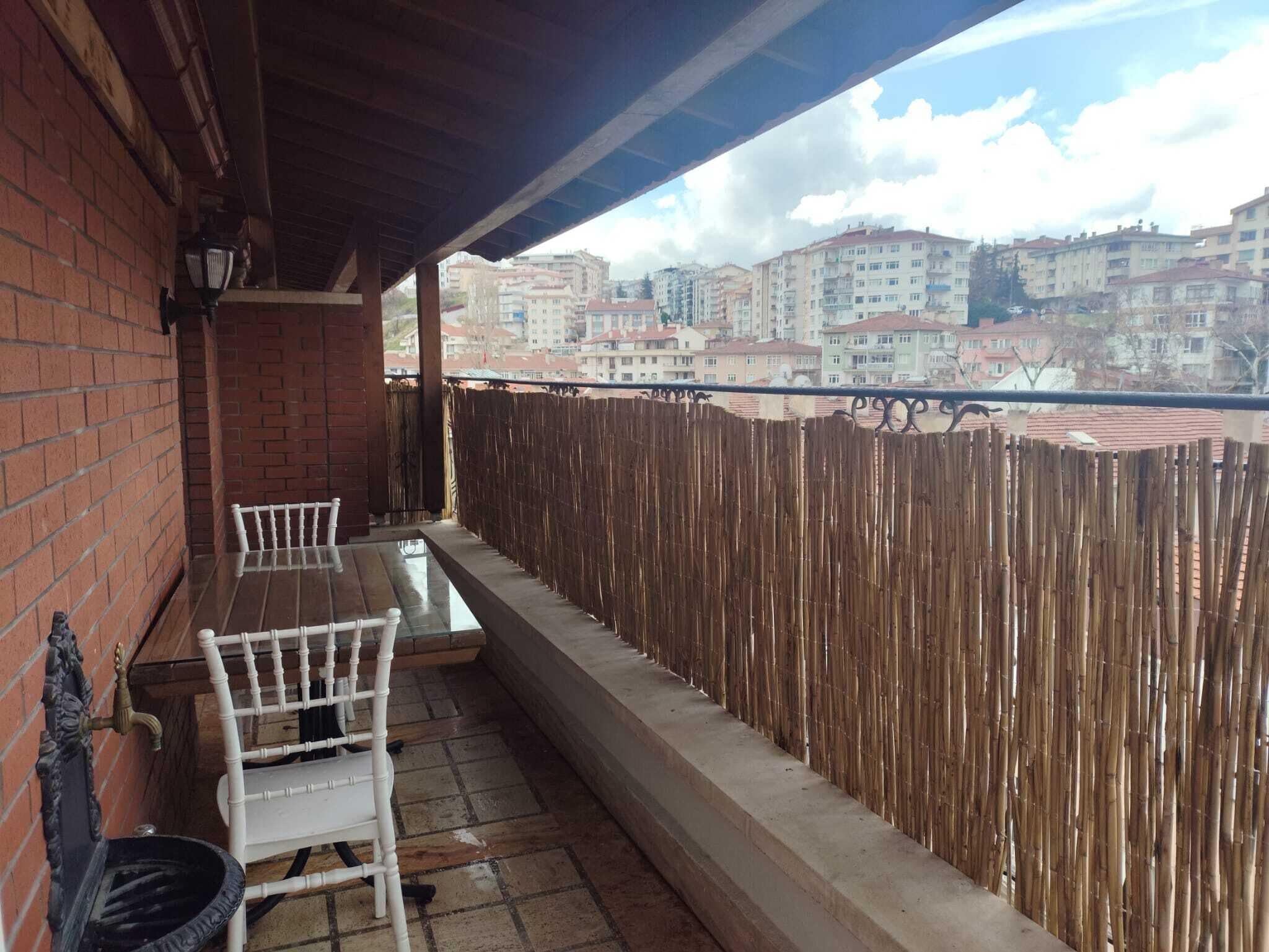 Een balkon met een tafel en stoelen, een bakstenen muur en een bamboescherm.