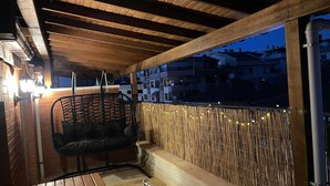 A covered outdoor seating area with a hanging chair, a bench, and a view of the cityscape at dusk. - Butik 24 Suites (Ankara)