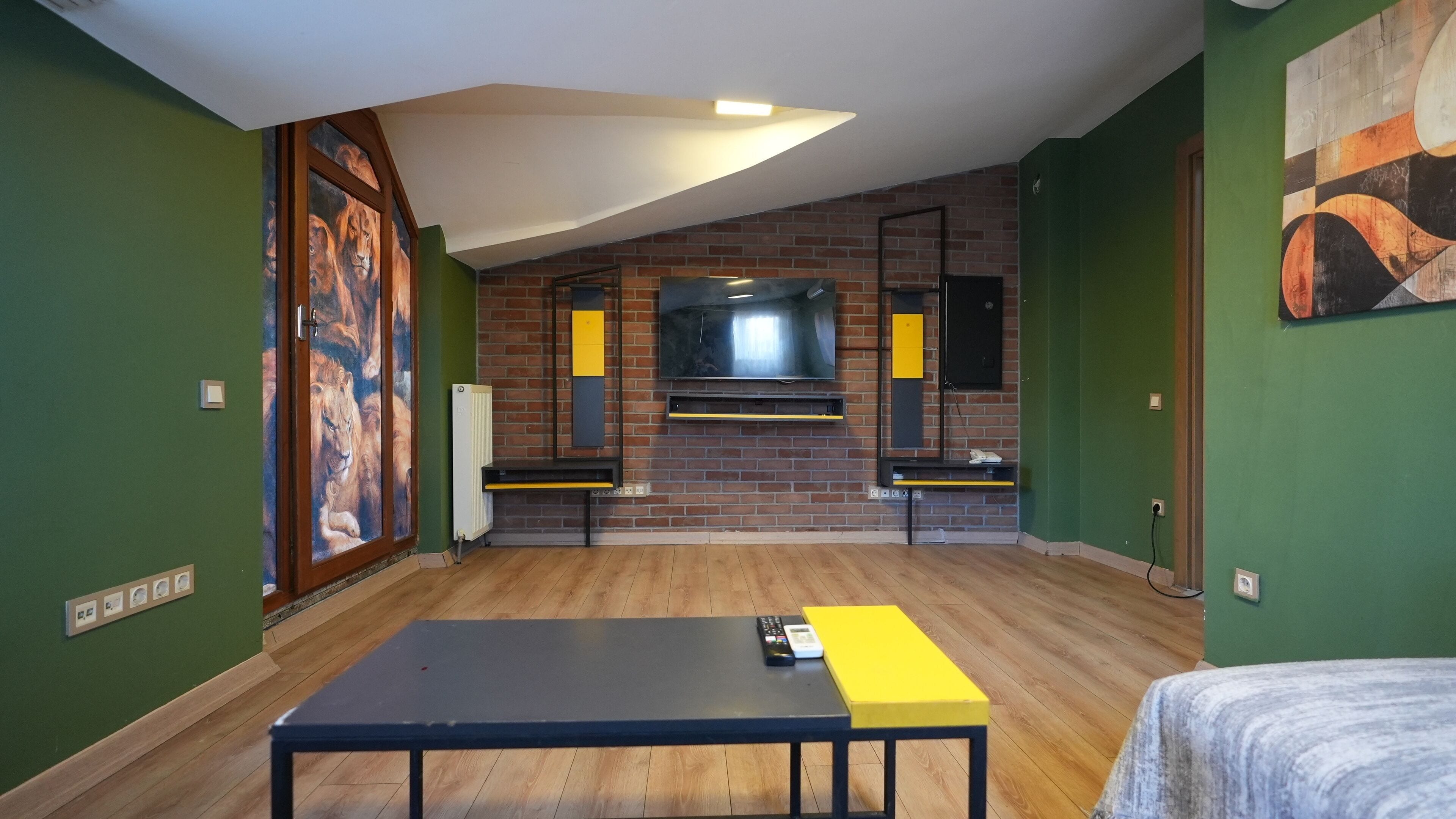 A room with a brick fireplace, a flat-screen TV mounted on the wall, and a large window.