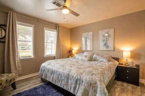 A bedroom with a bed, two bedside tables, a ceiling fan, and two windows with curtains. - BodhiTree Home - 3 Bedroom Bungalow (Houston)