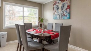 A dining area with a round table set for six, surrounded by grey upholstered chairs. - BodhiTree Home - 3 Bedroom Bungalow (Houston)