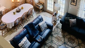 Un salon spacieux doté d’une grande fenêtre, un coin repas agrémenté d’un lustre, et un espace détente confortable avec un canapé bleu et un tapis à motifs.