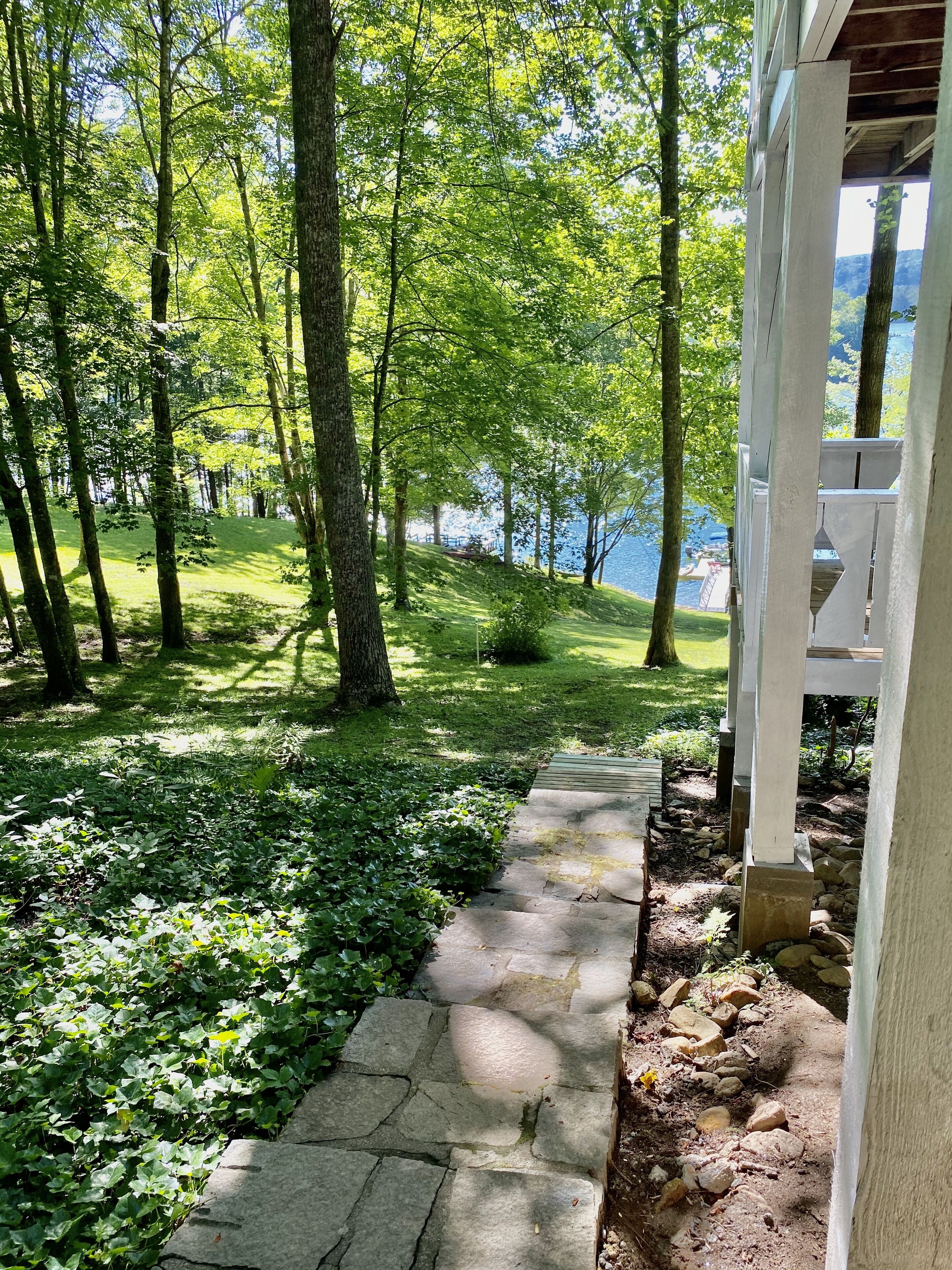 A stone pathway leading through a lush green area with trees and a view of a lake.