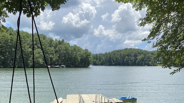 Une terrasse au bord du lac avec un fauteuil suspendu, une jetée s’avançant dans l’eau et un petit bateau.