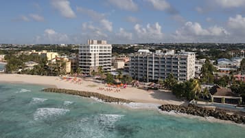 A coastal hotel with multiple buildings, a sandy beach, and clear turquoise waters.